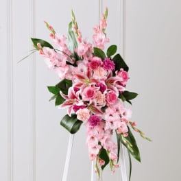 Tall pink standing floral spray on a white easel with roses, lilies, and carnations.