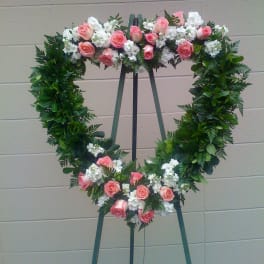 Heart-shaped floral wreath with pink roses and white flowers on an easel