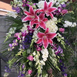 Tall standing spray with pink lilies, white flowers, purple blooms, and palm fronds on a wooden easel
