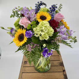 Mixed bouquet with sunflowers, roses, hydrangea and purple blooms in a clear glass vase