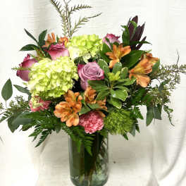 Mixed bouquet of green hydrangeas, pink roses and carnations, and orange alstroemeria in a glass vase