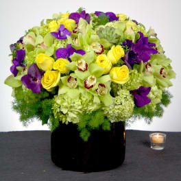 Low arrangement of green hydrangeas, yellow roses, and purple orchids in a black vase