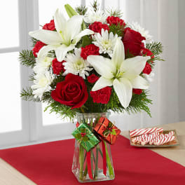 Red and white floral arrangement in a clear vase with small gift boxes