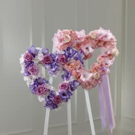 Two heart-shaped floral stands with pink and purple flowers and ribbons
