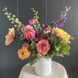 Mixed bouquet of pink, peach, yellow, and purple flowers in a white vase