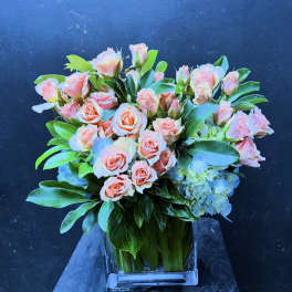 Peach roses and blue hydrangeas in a clear square vase