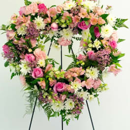 Heart-shaped floral wreath with pink and white flowers on a black stand