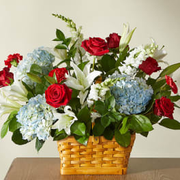 Basket arrangement of red roses, blue hydrangeas, and white lilies