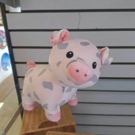 Small pink plush pig with gray spots displayed on a glass shelf.