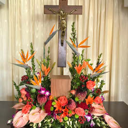 Large floral arrangement with orange birds of paradise and roses beneath a crucifix