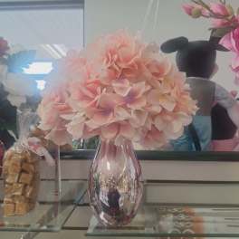 Pink hydrangea bouquet in a reflective vase on a glass shelf