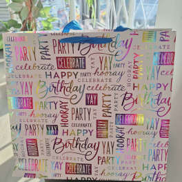 Birthday gift bag with colorful party words and blue tissue paper