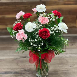 Bouquet of red, pink, and white carnations in a glass vase with a red ribbon