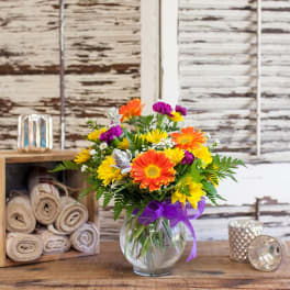 Colorful mixed bouquet in a clear glass vase with a purple ribbon