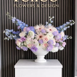 Pastel floral arrangement in a white urn with blue and lavender blooms