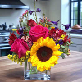 Bright mixed bouquet with sunflowers and pink roses in a clear glass vase