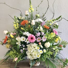 Large mixed flower arrangement in a woven basket with pink, white, yellow, and orange blooms