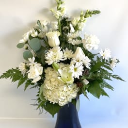 White floral arrangement in a dark vase with daisies, roses, and lilies