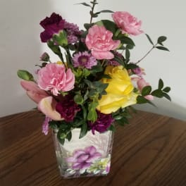 Mixed pink, purple, and yellow flowers in a clear square vase
