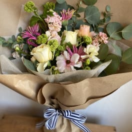 Hand-tied bouquet of pale roses and pink blooms wrapped in brown paper