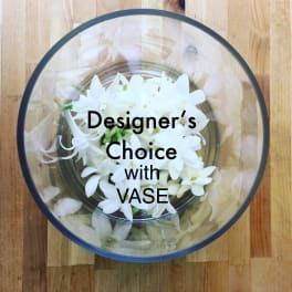 Round glass bowl filled with small white flowers viewed from above on a wooden surface.