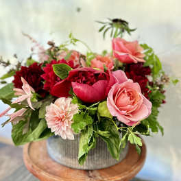 Low pink and red flower arrangement with roses and dahlias in a ribbed metal vase on a wooden stand
