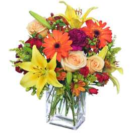 Bright mixed bouquet with lilies, roses, and orange daisies in a clear glass vase