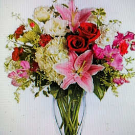 Mixed bouquet of pink lilies, red roses, and white flowers in a clear vase