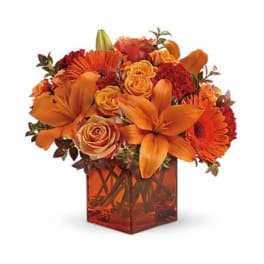 Orange and red mixed flower arrangement in a square glass vase