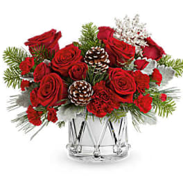 Red roses arranged in a clear glass vase with pinecones and winter greenery