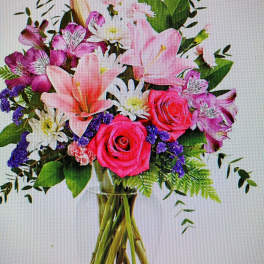 Mixed bouquet of pink roses, lilies, and purple flowers in a glass vase