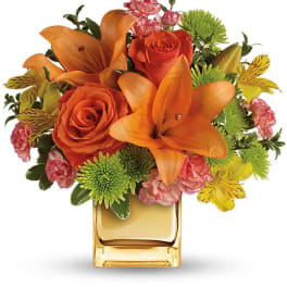Orange lilies and roses in a square glass vase