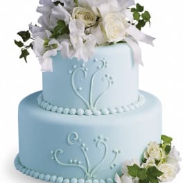 Two-tier blue cake with white floral topper and ribbon