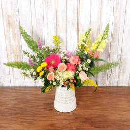 Asymmetrical mixed arrangement of pink, yellow and peach flowers in a white ceramic vase