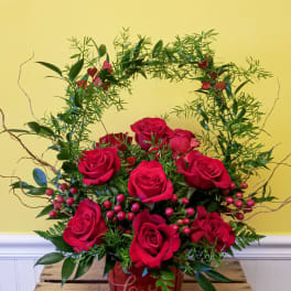 Red roses arranged in a red heart-shaped container with greenery