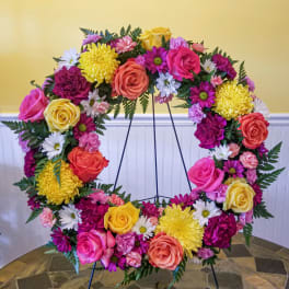 Large floral wreath on a stand with pink, yellow, white, and coral blooms