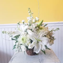 White floral arrangement in a wicker basket with lilies and chrysanthemums