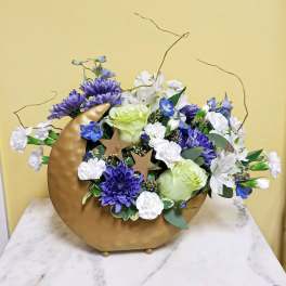 Purple and white floral arrangement in a gold crescent vase with star accents