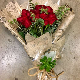 Bouquet of red roses wrapped in newspaper-style paper with eucalyptus and a succulent accent