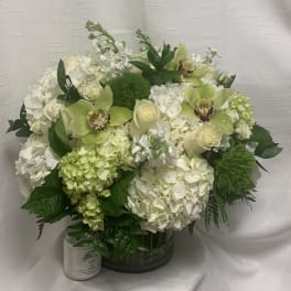Round arrangement of white hydrangeas, cream roses, and green orchids in a clear glass vase