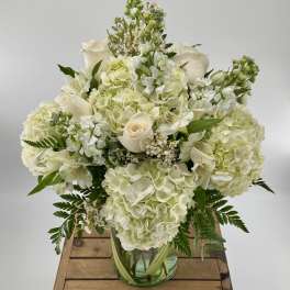 White hydrangeas and roses arranged with accent blooms in a clear glass vase.
