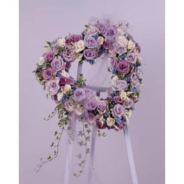 Heart-shaped wreath of lavender, purple, and cream roses on a white easel stand