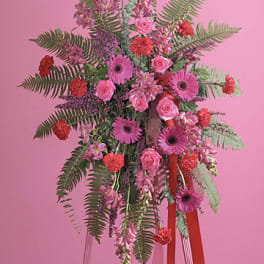 Tall pink and red standing spray with gerbera daisies, roses, carnations, and ferns on an easel.
