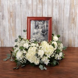 Low white floral arrangement surrounding a red photo frame with a black and white family picture.
