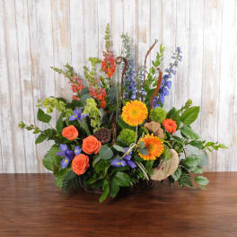 Large mixed arrangement with orange roses and gerberas, blue delphinium, and purple irises in a basket