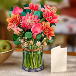 Paper pop-up bouquet of pink and orange flowers in a vase with a blank cream card beside it