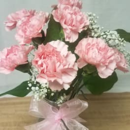 Pink carnations in a glass vase with a pink ribbon