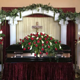 Casket spray and matching rose arrangements around a funeral casket