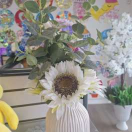 White sunflower arrangement in a ribbed vase with green foliage