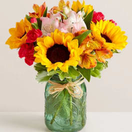 Bouquet of sunflowers, alstroemeria, and carnations in a green glass jar